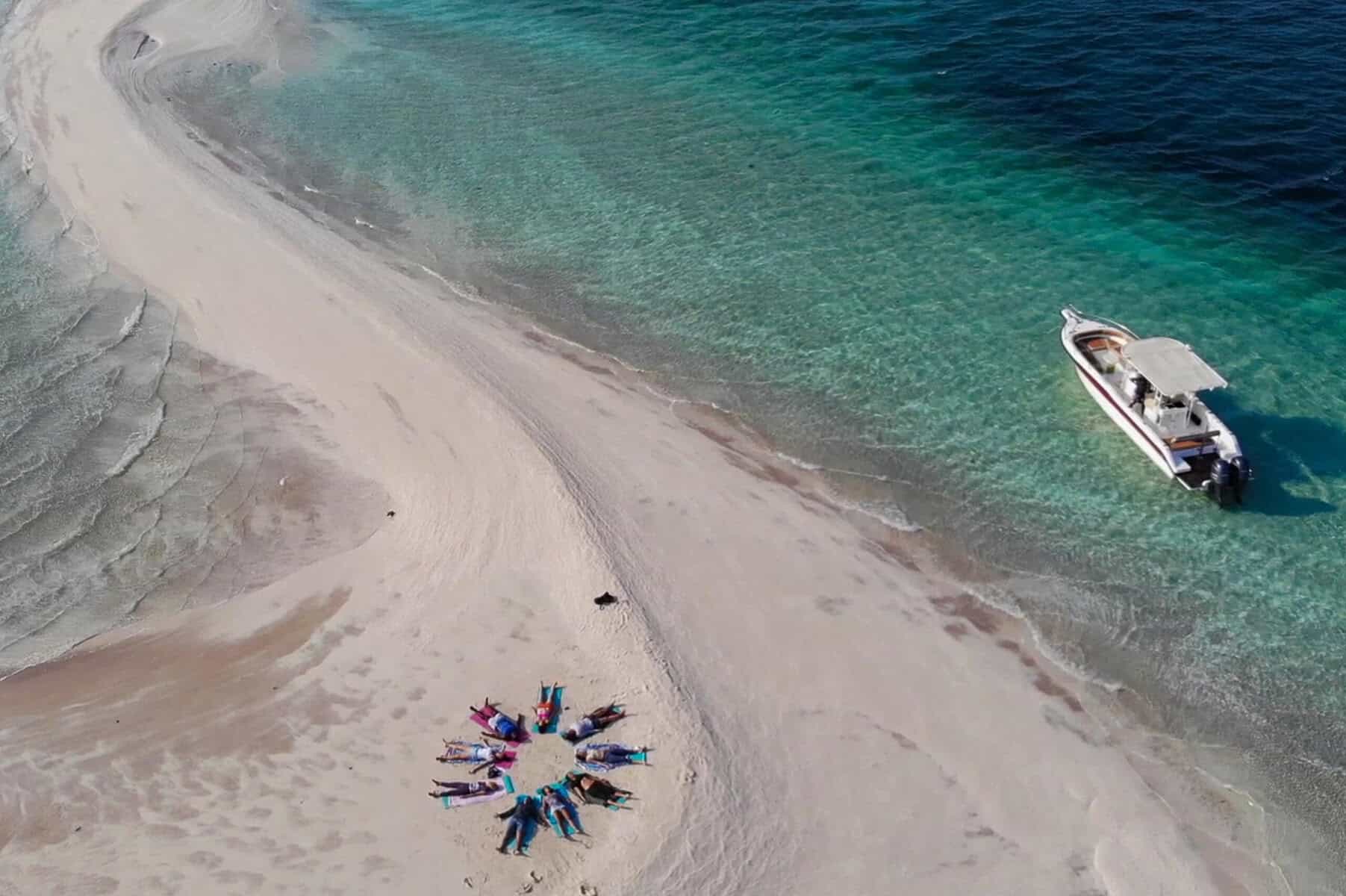 Beach with boat and sunbathers on the sand, tropical coastal scenery.