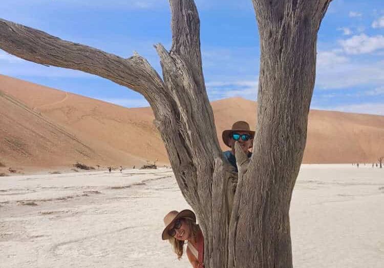 Family exploring desert landscape behind a tree.